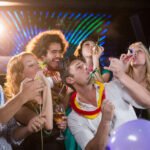 Group of smiling friends blowing party horn in bar